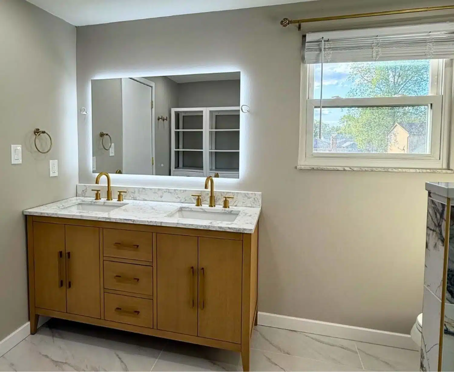 Modern bathroom vanity remodel - natural wood cabinets - marble look countertop - backlit mirror - gold fixtures - Columbus Ohio