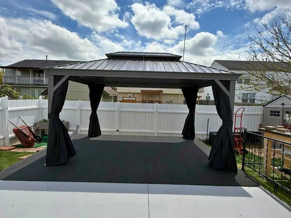 Gray metal gazebo with black curtains installed over a raised backyard patio area