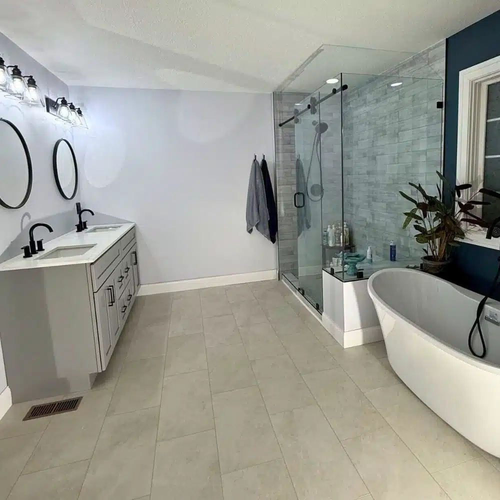 Contemporary bathroom remodel with freestanding soaking tub, glass walk-in shower, double vanity with black fixtures, and light gray tile flooring