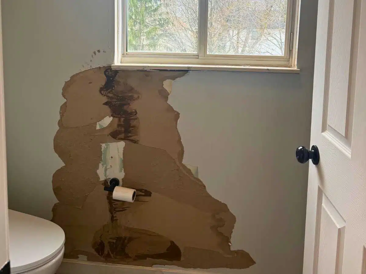 Before - bathroom wall with severe water damage below the window and exposed drywall around the toilet area