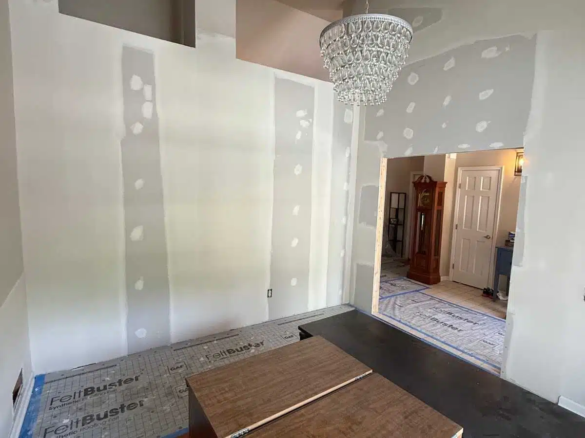 Before - room with unfinished drywall repairs visible on the walls and protective floor covering in place