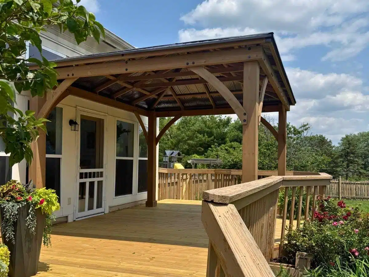 Covered wood patio gazebo attached to the house with decorative beams and metal roof over a backyard deck
