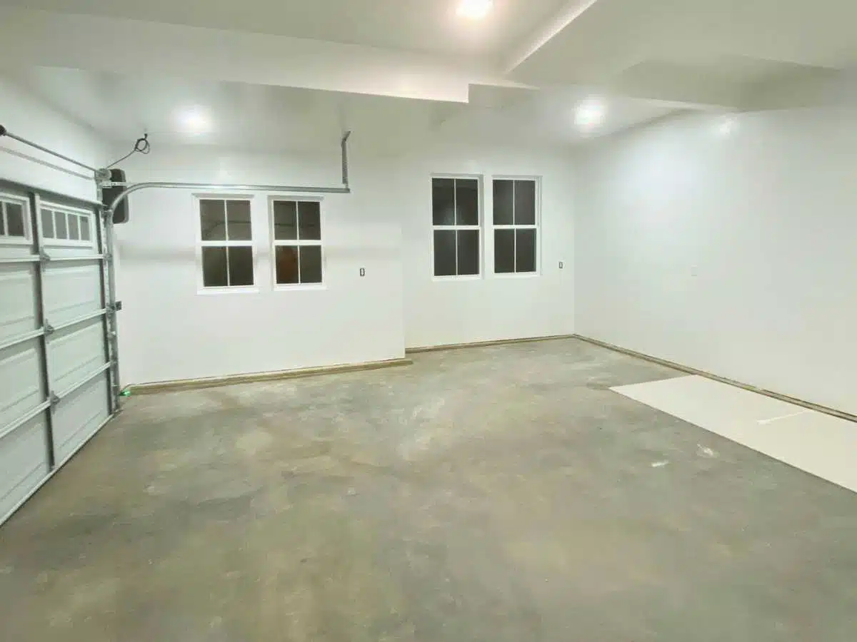 newly drywalled garage interior with smooth white walls recessed lighting and clean concrete floor