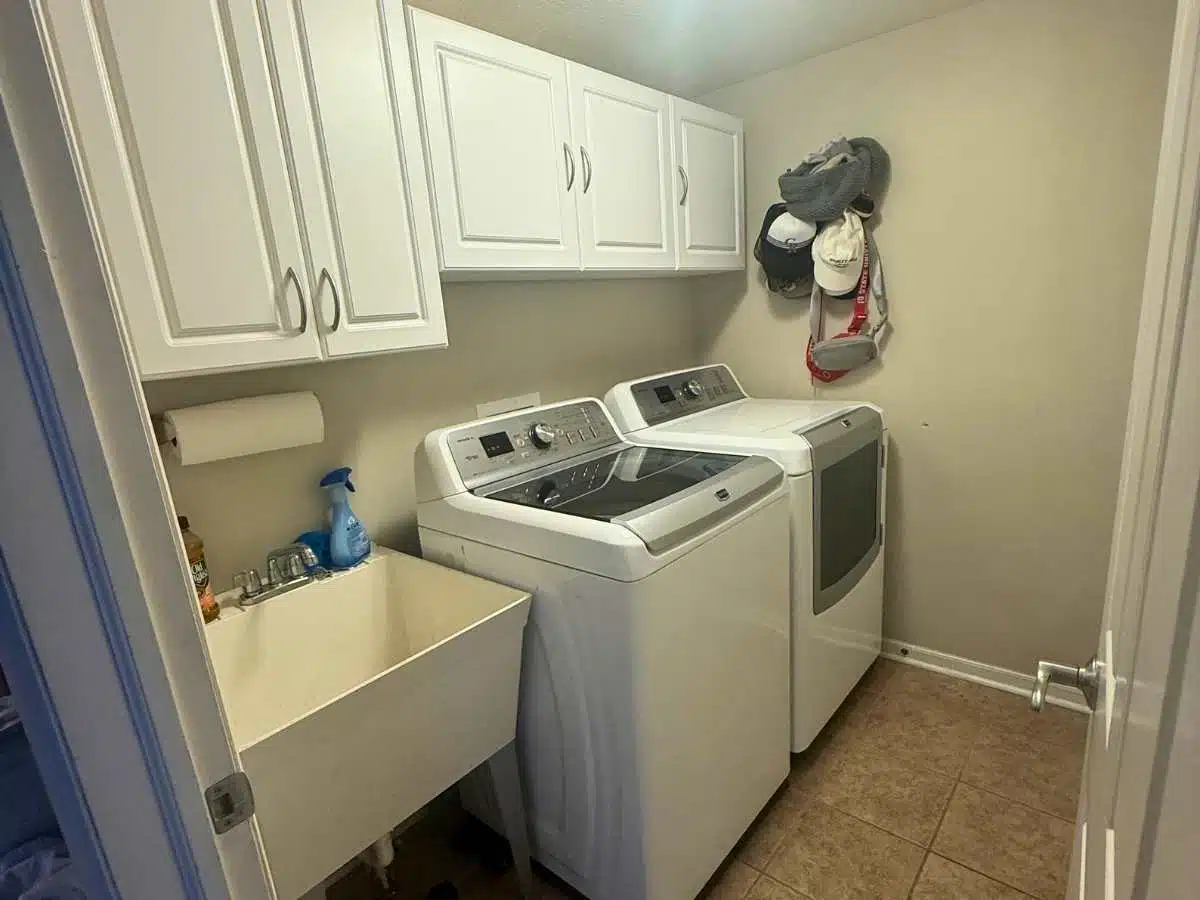 Laundry room before renovation with white appliances and utility sink