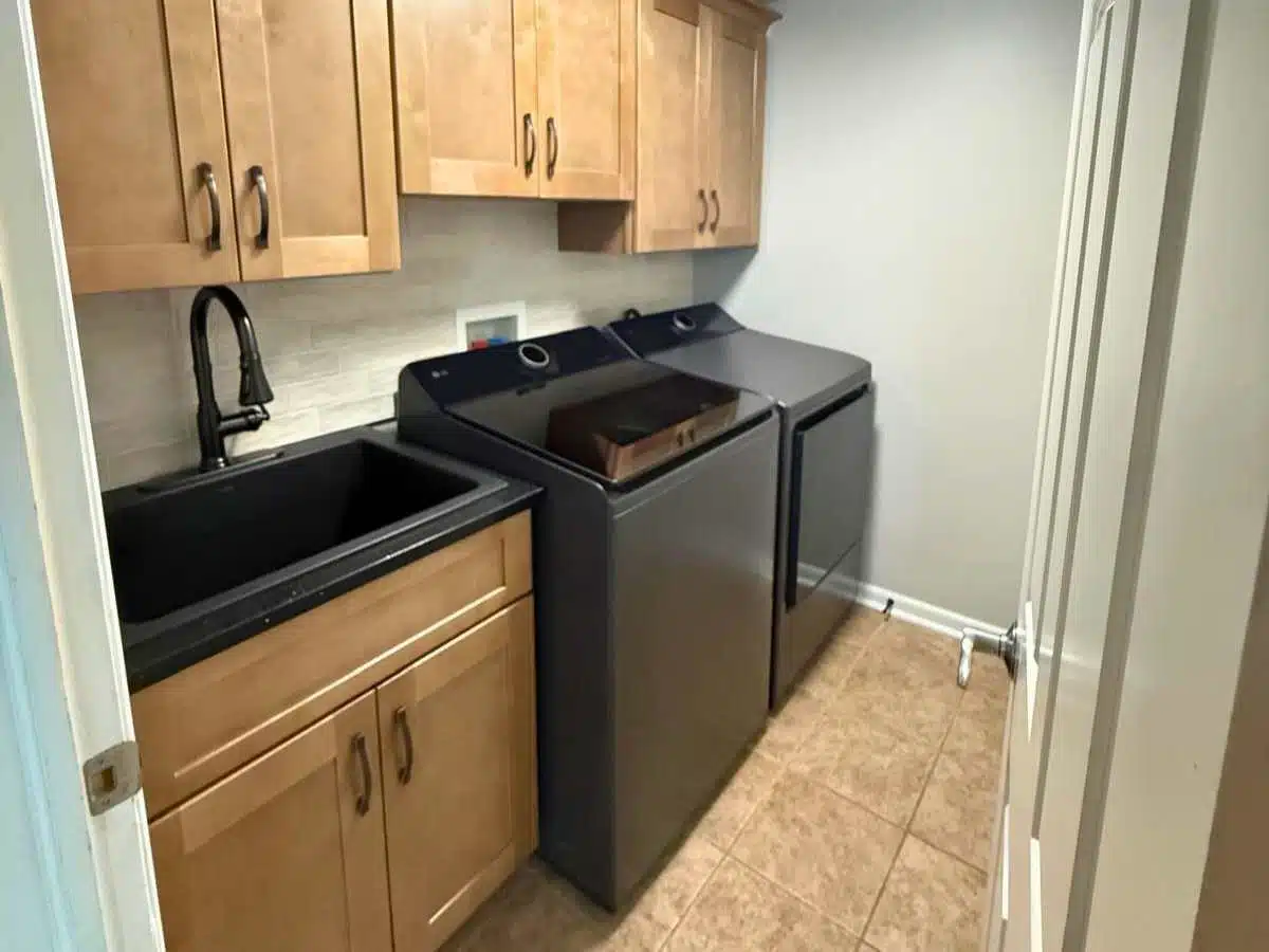 Remodeled laundry room with cabinets, utility sink and black appliances